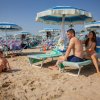 Famiglia in spiaggia sotto ombrelloni blu e bianchi.
