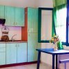 Cucina con pensili verde acqua, tavolino blu con vaso di fiori e finestra con tenda verde.