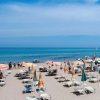 Spiaggia sabbiosa con ombrelloni colorati e sdraio, vista mare blu e cielo sereno.