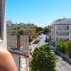 Vista su una strada cittadina da un balcone, con palazzi e alberi lungo la via.