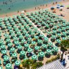 Numerosi ombrelloni verdi disposti ordinatamente sulla sabbia vicino al mare.