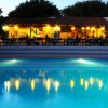 Piscina illuminata di notte con ristorante sullo sfondo.