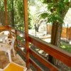 Veranda esterna in legno con tavolo e sedie bianche, immersa nel verde.