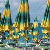 Ombrelloni a righe verdi e gialle su una spiaggia affollata con il mare sullo sfondo.
