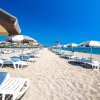 Spiaggia sabbiosa con file di lettini e ombrelloni sotto un cielo blu.