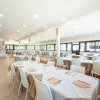 Ampia sala ristorante con tavoli apparecchiati e sedie bianche.