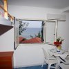 Interno di una stanza con tavolo e sedie. La finestra aperta offre vista sul mare.