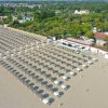 Spiaggia con file di ombrelloni e strutture verdi circostanti.
