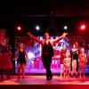 Persone sul palco che si esibiscono con luci rosse e uno sfondo decorativo.