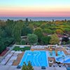 Vista dall'alto di una piscina e spa con lettini, circondata da alberi e un panorama al tramonto.