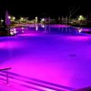 Piscina illuminata di notte con luci viola e sedie a sdraio circostanti.