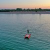 Persona su pedalò rosso in mare al tramonto con spiaggia sullo sfondo.