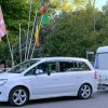 Auto bianca che traina una roulotte, vicino a bandiere e alberi verdi.