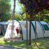 Una tenda da campeggio bianca e verde tra alberi e erba in un'area soleggiata.
