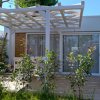 Bungalow con pergolato, circondato da piante e alberi.