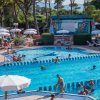 Piscina affollata con ombrelloni e scenografia sullo sfondo.