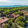 Resort con edifici dal tetto rosso circondato da pini e palme, vicino al mare.
