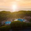 Tramonto su un complesso con piscine e alberi vista mare.