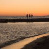 Tre persone camminano su una spiaggia al tramonto, con il mare sullo sfondo.