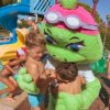 Mascotte verde abbraccia bambini vicino a uno scivolo d'acqua.