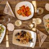 Tavolo di legno con piatti di pasta, pane e bicchieri di vino.