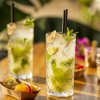 Due bicchieri di cocktail con lime e menta su un tavolo di legno, accanto a stuzzichini.