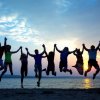 Persone che saltano tenendosi per mano al tramonto su una spiaggia.