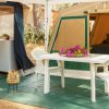 Esterno di una tenda da campeggio con tavolo e sedie bianche, fiori su tavolo, mini frigo in vista.