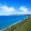 Una costa con mare blu e colline verdi sotto un cielo sereno.