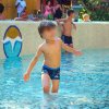 Un bambino sfocato gioca in una piscina poco profonda con persone sullo sfondo.