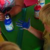 Bambino con la mano dipinta di blu osserva il colore. Sul tavolo ci sono bottiglie di vernice.