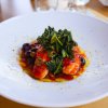 Piatto bianco con cibo decorato: verdure verdi su salsa rossa, accompagnate da condimenti e olio.