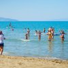 Spiaggia affollata con persone che giocano in acqua limpida. Mare azzurro e cielo sereno.