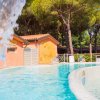 Piscina con cascata d'acqua, circondata da alberi e un edificio arancione sullo sfondo.