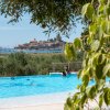 Piscina all'aperto con vista su un villaggio costiero in lontananza, e foglie verdi in primo piano.