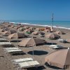 Spiaggia con file di ombrelloni e lettini sotto un cielo blu.