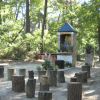 Un'edicola con statue, circondata da tronchi usati come sedili nel bosco.