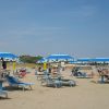 Una spiaggia sabbiosa con ombrelloni blu e lettini, persone rilassate sotto il sole.