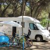 Camper e tende tra gli alberi in un campeggio, con biciclette parcheggiate davanti.