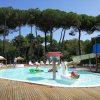Piscina con giochi gonfiabili e scivolo circondata da alberi e lettini.