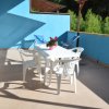 Ampia terrazza con tavolo e sedie bianche, pianta su tavolo, diverse sedie a sdraio blu.