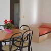 Stanza luminosa con tavolo di legno, sedie nere e un letto singolo con coperta arancione.