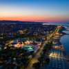 Spiaggia al tramonto con file di ombrelloni e luci accese lungo la costa.