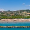 Spiaggia con ombrelloni, mare e colline sullo sfondo.