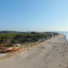 Ampia spiaggia con pochi ombrelloni, lungo un tratto di costa alberato e soleggiato.