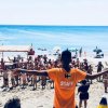 Persona in maglietta arancione guida un gruppo su una spiaggia.