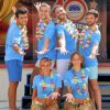 Sei persone sorridenti con magliette blu e collane di fiori.