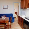 Cucina con tavolo in legno, sedie, divano blu e televisione. In fondo, una camera da letto.