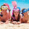 Tre bambini con maschere da snorkeling sdraiati sulla spiaggia.