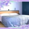 Camera d'albergo con letto matrimoniale e copriletto blu, contornata da cornice floreale viola.